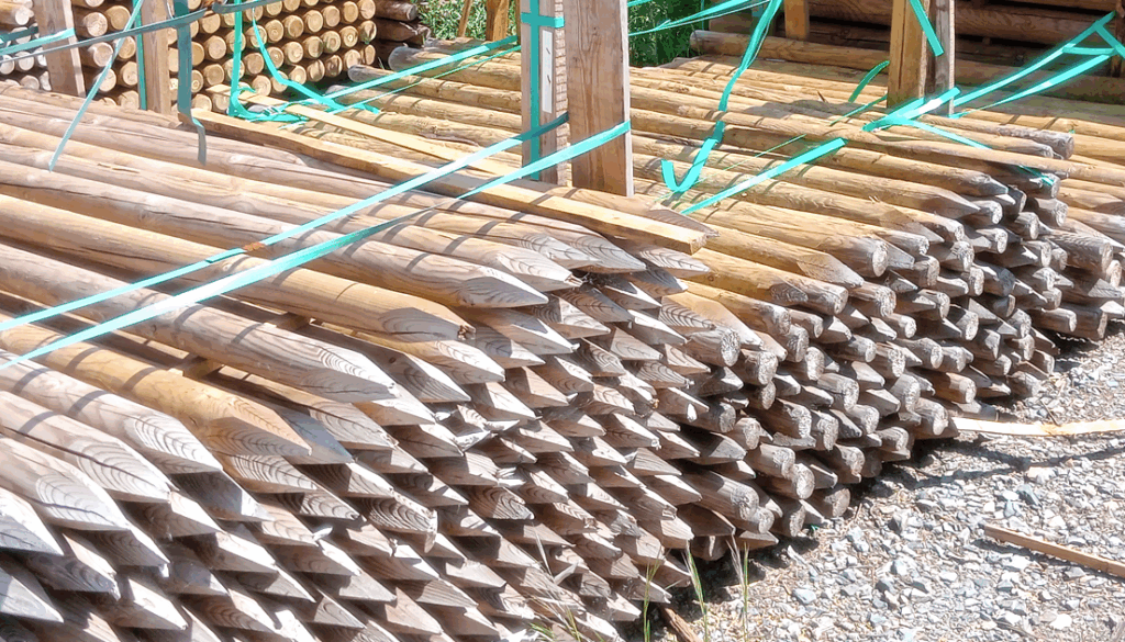 Postes de madera tratada apilados y sujetos con cintas en las instalaciones de Comercial Amador en Lalín.
